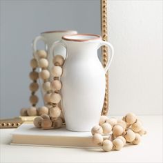 a white vase sitting on top of a table next to a mirror and wooden beads