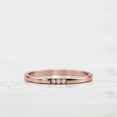 a rose gold wedding band with three diamonds on the top and bottom, sitting on a marble surface