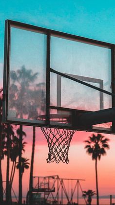 a basketball hoop with palm trees in the background and a pink sky at sunset behind it