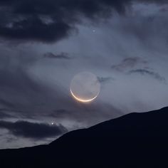 two crescents are seen in the night sky over a mountain range with dark clouds