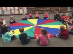 children sitting on the floor in front of a large colorful umbrella with people around it