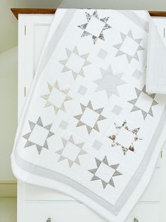 a white quilt with silver stars on it sitting on top of a dresser next to a pair of scissors