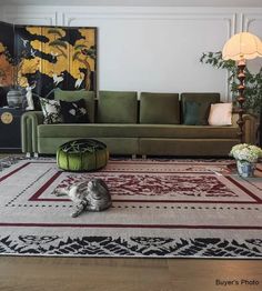 a cat sitting on the floor in front of a green couch and rug with flowers