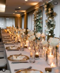 a long table is set with candles and flowers in glass vases, plates and silverware