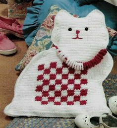 a crocheted white cat with a red tie on it's neck sitting next to some shoes