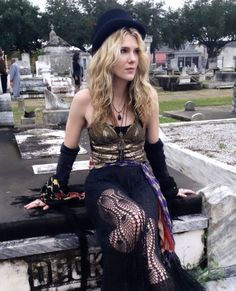 a woman sitting on top of a stone wall next to a cemetery wearing a black hat