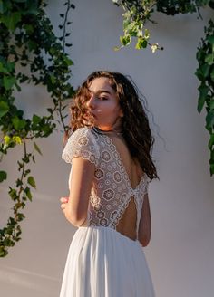 a woman wearing a white dress standing in front of a wall with ivy growing on it