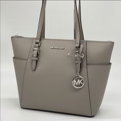 Brand New With Tag Michael Kors Charlotte Large Top Zip Tote Color: Pearl Grey Silver Toned Hardware 2 Slip-In Back Pocket On Side Pvc Leather With Pebbled Leather Trim 1 Mk Circle Charm Zip Top Closure Custom Fabric Lining Interiors: 2 Slip-In Pockets And 1 Zipped Pocket 15"(Top) 11"(Bottom) X 10"(H) X 4.5"(D) Straps: 9.5" Dust Bag Not Included Modern Travel Bag With Silver-tone Logo, Modern Travel Bags With Silver-tone Logo Plaque, Modern Travel Bag With Silver-tone Logo Plaque, Classic Shoulder Bag With Silver-tone Logo Plaque, Silver-tone Logo Plaque Shoulder Bag, Shoulder Bag With Silver-tone Logo Plaque For Everyday Use, Chic Bags With Silver-tone Logo Plaque For Everyday Use, Everyday Silver Bags With Branded Hardware, Michael Kors Silver Shoulder Bag With Branded Hardware