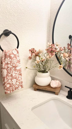 a white sink sitting under a bathroom mirror next to a vase with flowers in it