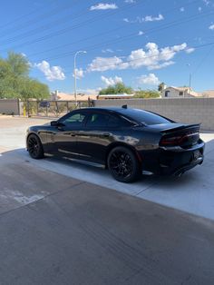 a black sports car parked in a parking lot next to a wall and fenced off area