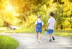 two young boys walking down a road holding hands and looking at the sun behind them