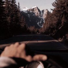 a person is driving down the road with their hand on the steering wheel and mountains in the background