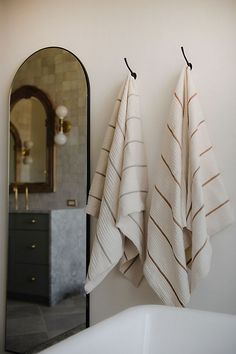 two towels hanging on the wall next to a bathtub and mirror in a bathroom