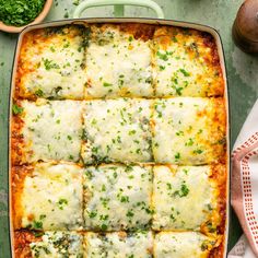 a casserole dish with cheese and parsley in it on a green table