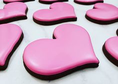 pink and black heart shaped cookies sitting on top of a white table covered in frosting