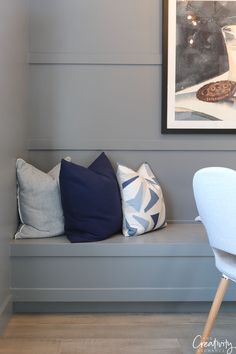 a bench with several pillows on it in front of a painting and chair next to it