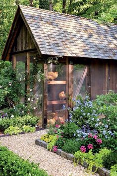 a chicken coop with chickens in it surrounded by flowers and plants on either side of the building