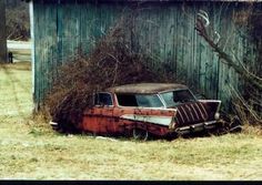 an old rusted car sitting in front of a wooden fence