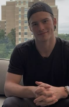 a man sitting on top of a couch in front of a window with his hands crossed