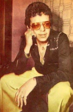 an old photo of a man in sunglasses sitting on a chair with his hand to his ear