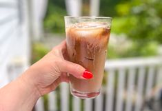 a hand holding a glass with liquid in it and a red manicure on the tip