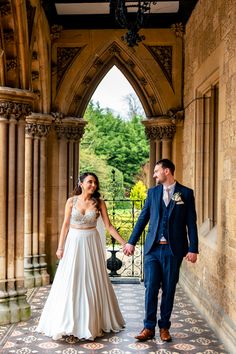 a bride and groom hold hands as they walk through an archway