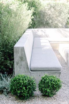 a concrete bench sitting in the middle of a gravel area next to bushes and shrubbery