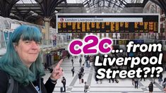 a woman with blue hair is pointing at the camera in front of a train station