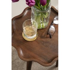 purple flowers in a glass vase on a wooden table with eyeglasses next to it