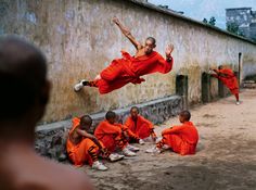 a group of men sitting on the ground in front of a wall with their hands up