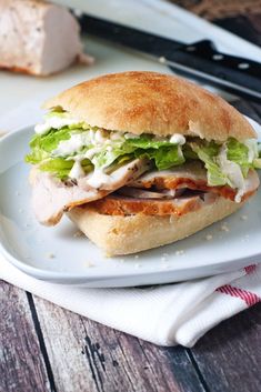 a sandwich with meat, lettuce and cheese on a plate next to a knife