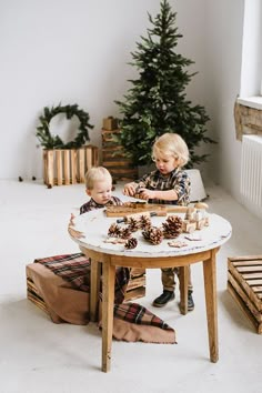 two young boys playing with pine cones on a table in front of a christmas tree