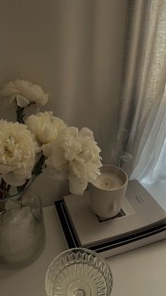 a vase filled with white flowers sitting on top of a table next to a book