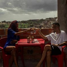 a man and woman sitting at a red table on top of a roof next to each other