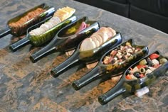 five wine bottles filled with different types of food on a table top, all lined up in the same row