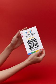 a person holding up a white card with qr code on it in front of a red background