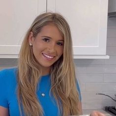 a woman is smiling and holding a pizza in her hands while sitting at the kitchen counter