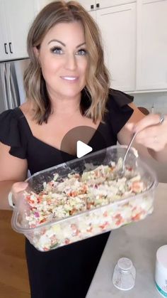 a woman in a black dress is holding a plastic container with food on it and she is smiling at the camera