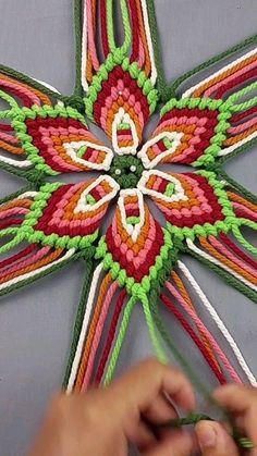 a person is working on a colorful flower design with crocheted threads and yarn