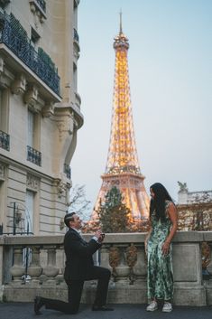 a man kneeling down next to a woman in front of the eiffel tower