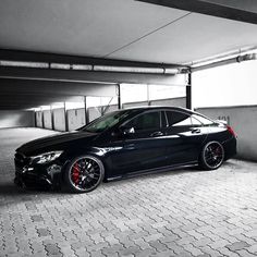 a black car parked in an empty parking garage with red rims on the tires