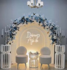 two white chairs sitting next to each other in front of a wall with flowers on it