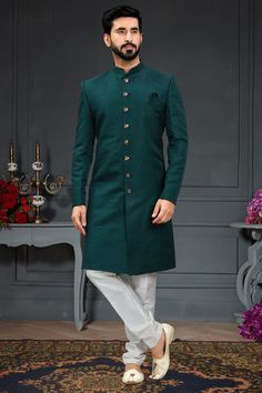 a man in a green sherwa with white pants and tan shoes standing on a rug