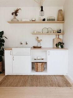 a white kitchen with open shelves and baskets on the counter top, next to a potted plant