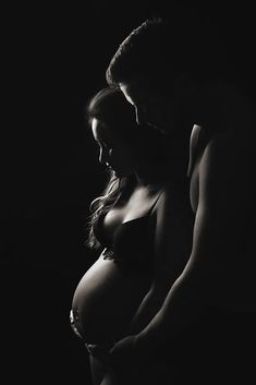 black and white photograph of a pregnant woman with her husband looking at her belly in the dark