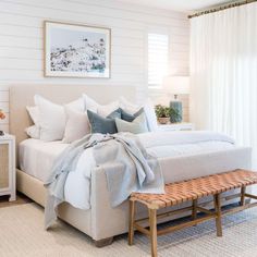 a bed with white sheets and pillows in a bedroom next to a wooden foot board