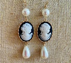 An ultra-feminine flirty pearl cameo dangle earring with a pearl up top and a teardrop pearl at the bottom: a beautiful white cameo on a jet black background in a gold frame, guaranteed to get compliments this season! We want you to look beautiful, but keep your savings account, too: Our U.S. FREE SHIPPING guarantees your jewelry budget isn't eaten up by postage.  Queen Victoria's love for cameos significantly increased their popularity in the 19th century as they became symbols of status and el Vintage Cameo Jewelry, Black Cameo, Bridesmaids Earrings, Cameo Earrings, Vintage Style Earrings, Island City, Ultra Feminine, Cameo Jewelry, Fashion Institute