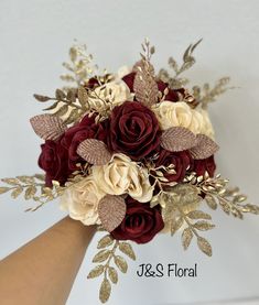 a bridal bouquet with red roses and gold leaves on the wristlet is being held by a woman's hand