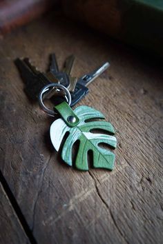 a green leaf shaped keychain sitting on top of a wooden table next to two keys