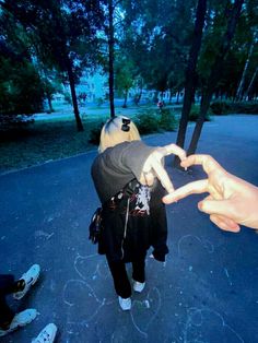 two people standing in the middle of a road making a heart shape with their hands